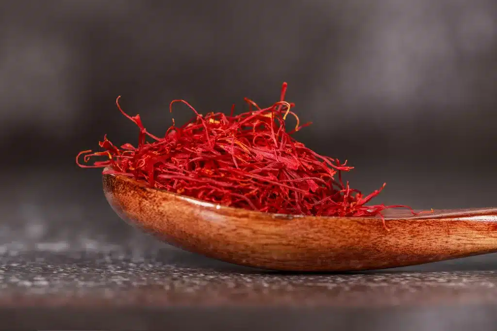 A close-up view of saffron threads arranged in a small pile. The threads are slender and vibrant, displaying a beautiful combination of bright red and pale yellow colors.